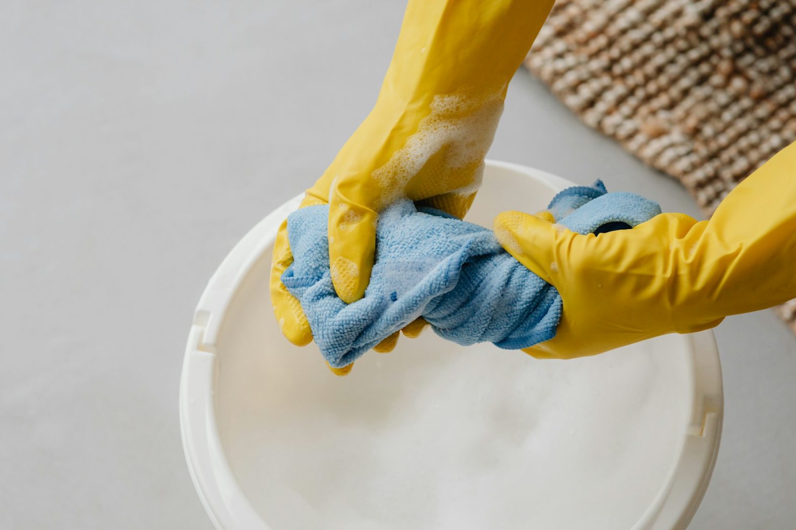Hands wearing yellow gloves wringing out a blue cleaning cloth over a bucket filled with soapy water, symbolizing the use of Sisel International's safe, non-toxic home care products for effective and environmentally friendly cleaning routines.