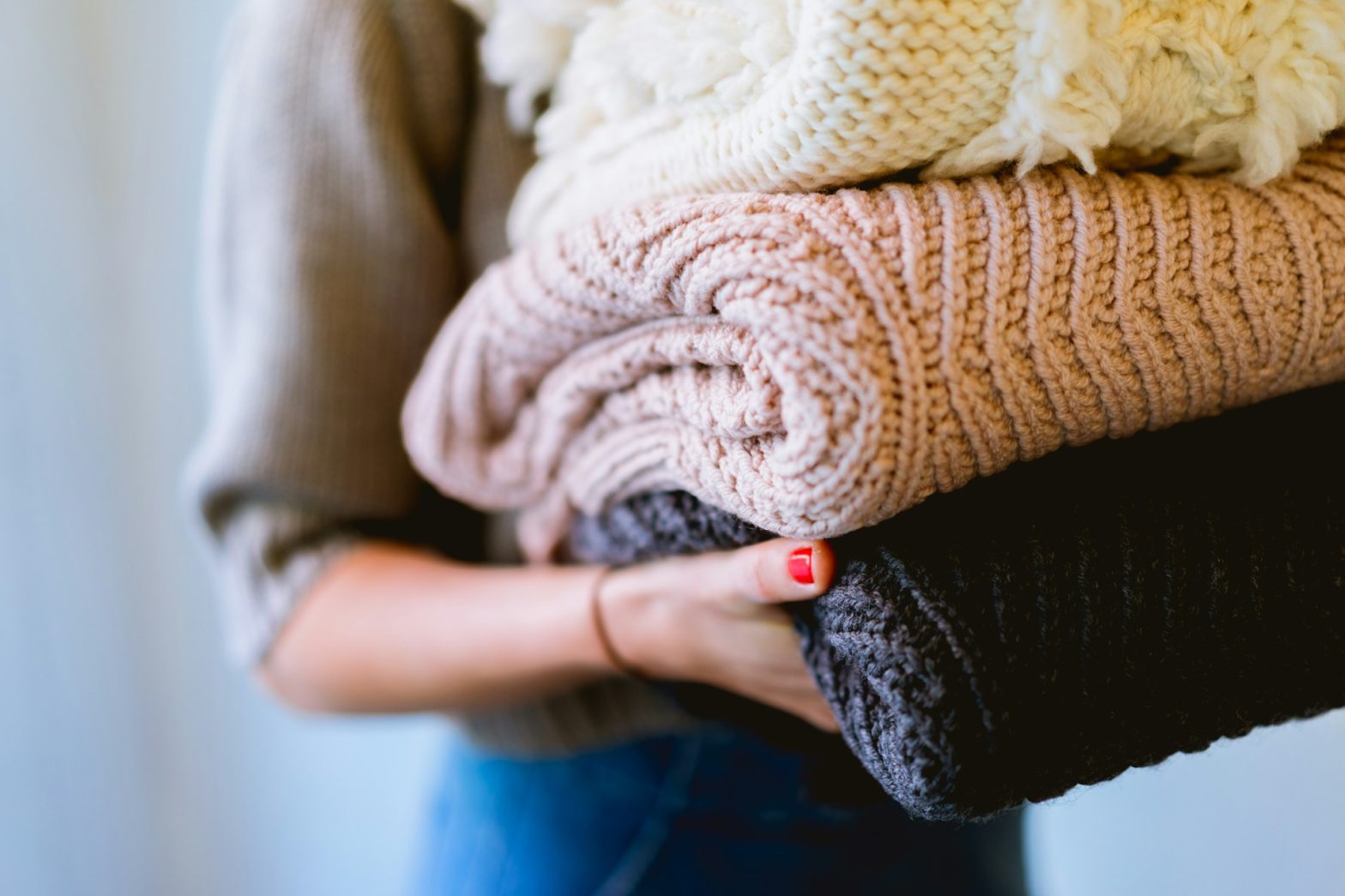 Close-up of a person holding a stack of freshly laundered knit blankets, symbolizing the warmth and comfort of eco-friendly, non-toxic laundry products like Sisel's Vibrant™ Laundry Detergent. A sustainable choice for keeping fabrics clean and safe for the home environment.