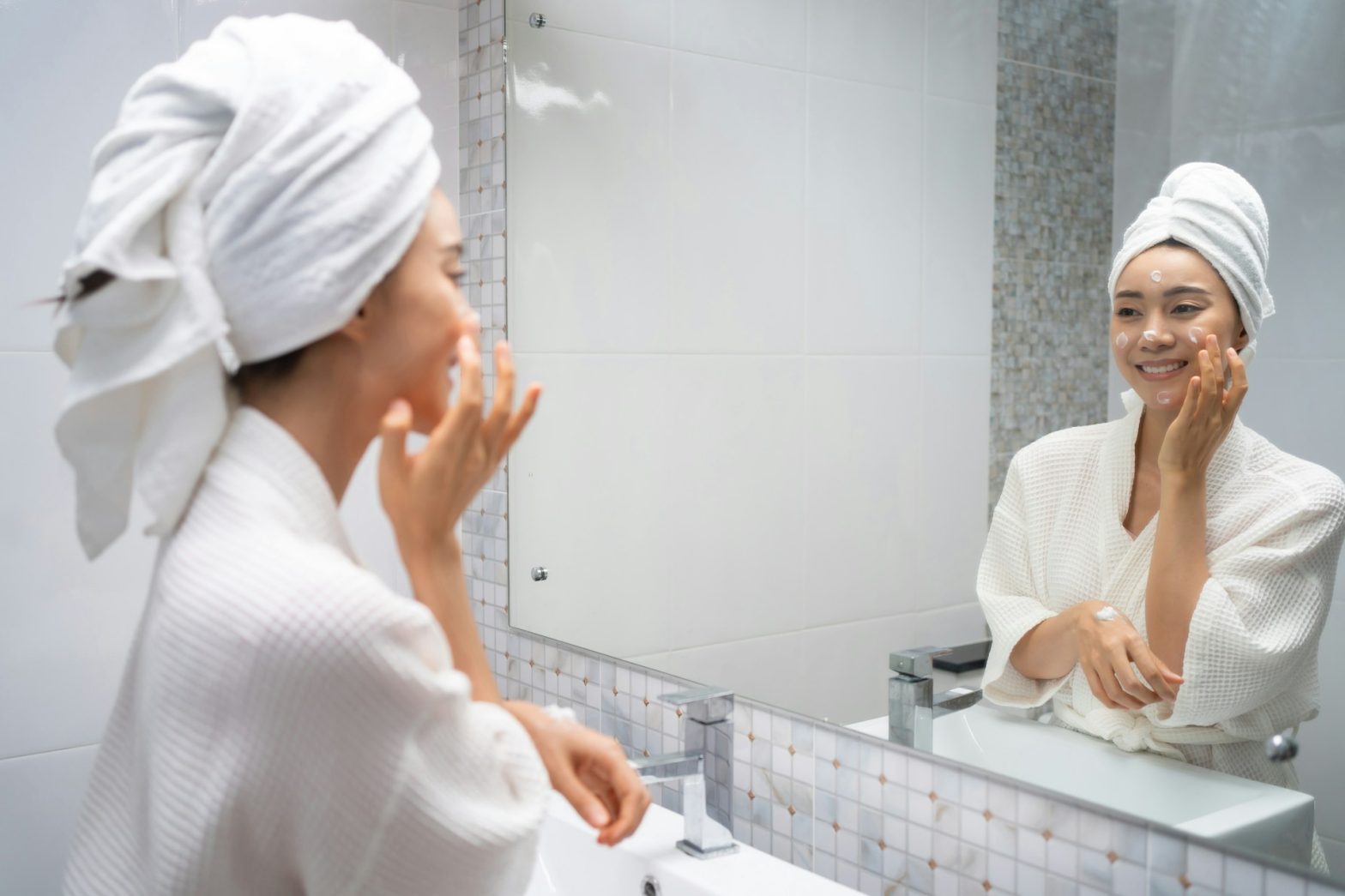 A woman applies skincare cream while smiling at her reflection, illustrating the use of personal care solutions for a natural beauty routine.